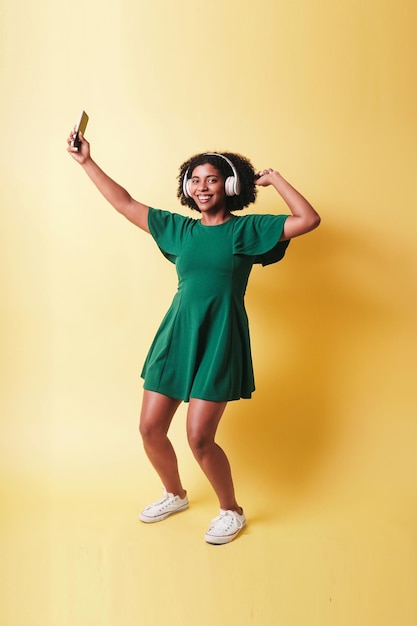 Foto joven negra sostiene un teléfono inteligente con auriculares escuchar música y bailar