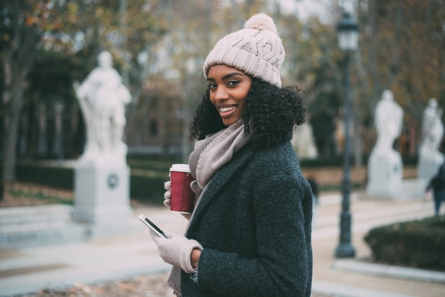 Joven negra tomando café y hablando por teléfono móvil cerca del palacio real en invierno