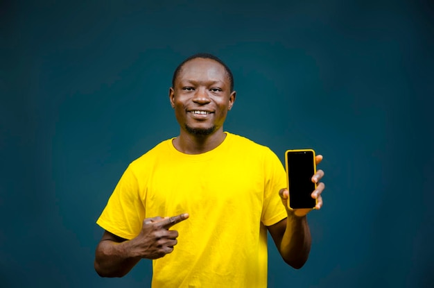 Joven negro africano sosteniendo y señalando su teléfono móvil mientras mira a la cámara