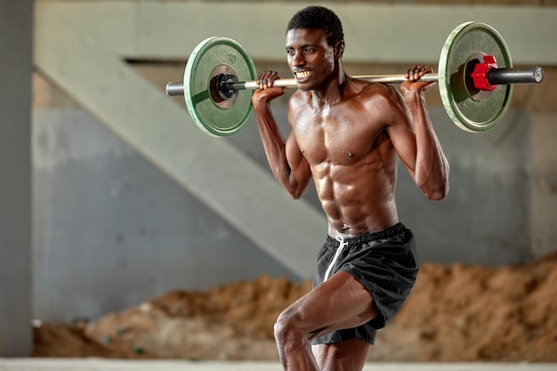 Joven negro atlético levantando una pesa pesada en un gimnasio al aire libre bajo el puente Concepto de estilo de vida saludable