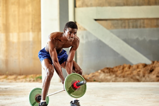 Joven negro atlético levantando una pesa pesada en un gimnasio al aire libre bajo el puente Concepto de estilo de vida saludable