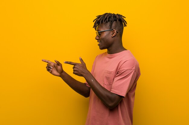 Joven negro casual con gafas de sol excitado apuntando con los dedos lejos.