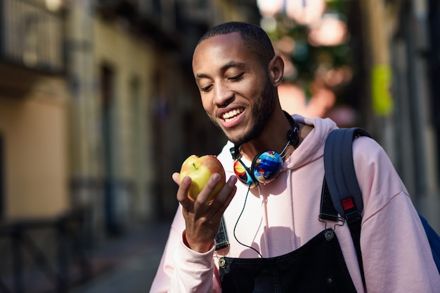 Joven negro comiendo una manzana caminando por la calle.