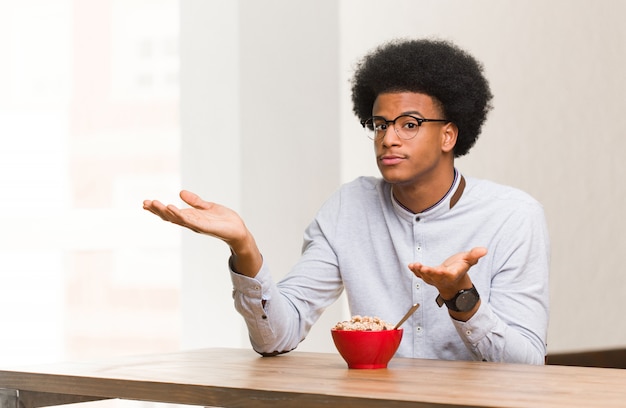 Joven negro desayunando confuso y dudoso