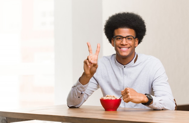 Joven negro desayunando mostrando el número dos