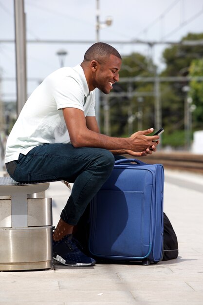 Joven negro esperando en la estación de ferrocarril con teléfono