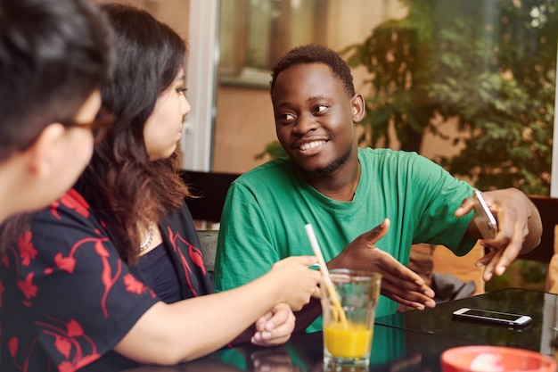 joven negro explica algo a sus amigos en una mesa