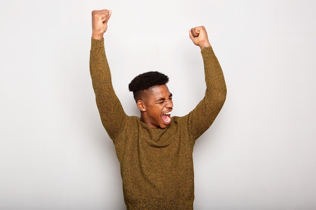 joven negro feliz con los brazos levantados de alegría contra un fondo gris