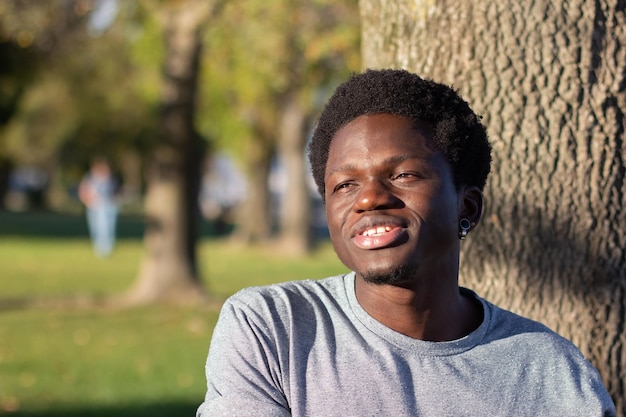 Joven negro pasando tiempo al aire libre en el parque de la ciudad. Guapo hombre afroamericano en camiseta gris casual mirando a un lado y hablando. Tiro medio. Juventud, estilo de vida, concepto de tiempo libre.