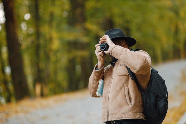 Joven negro de pie en la carretera en el bosque con una cámara. Fotógrafo masculino tomar una foto