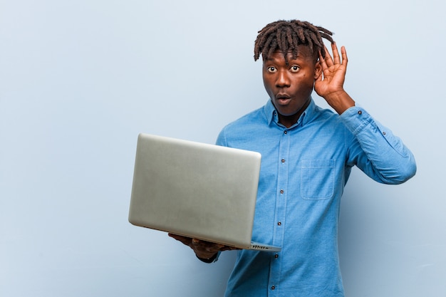 Joven negro rasta sosteniendo un portátil tratando de escuchar un chisme.