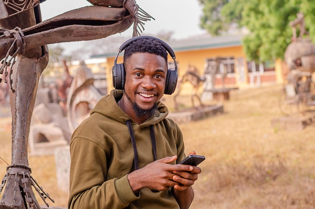 Joven negro relajándose al aire libre escuchando música usando el teléfono y los auriculares Copiar espacio