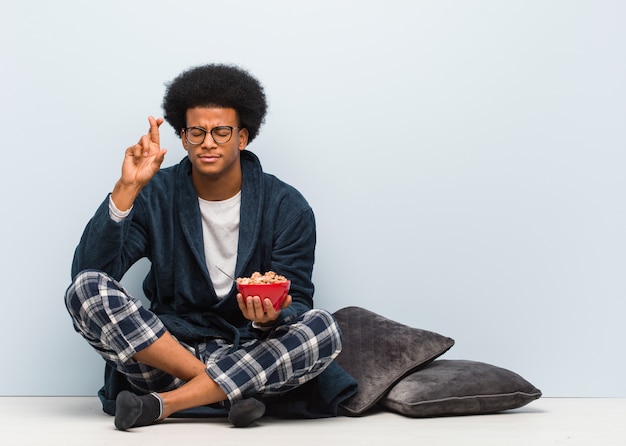 Joven negro sentado y desayunando cruzando los dedos para tener suerte