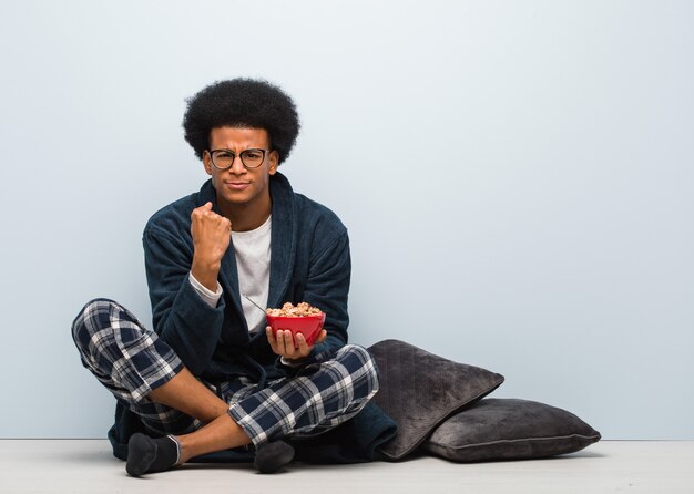 Joven negro sentado y desayunando mostrando el puño al frente, expresión enojada