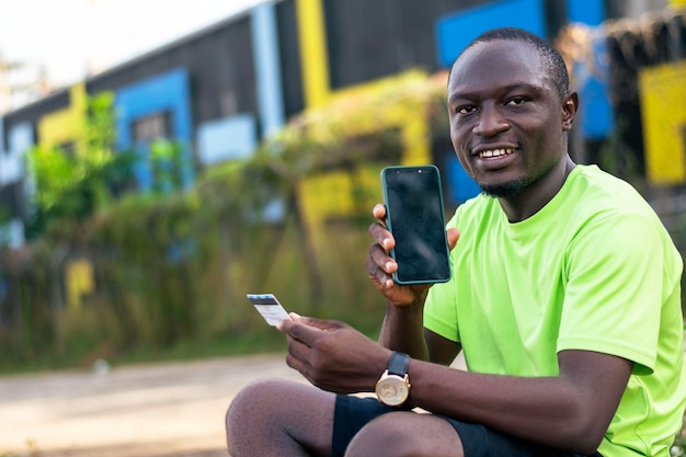 Un joven negro sentado en el suelo sosteniendo un teléfono celular.