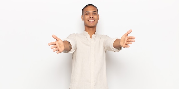 Joven negro sonriendo alegremente dando un cálido, amistoso y amoroso abrazo de bienvenida, sintiéndose feliz y adorable