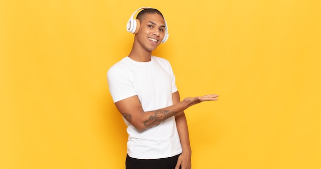 Joven negro sonriendo alegremente, sintiéndose feliz y mostrando un concepto en el espacio de la copia con la palma de la mano