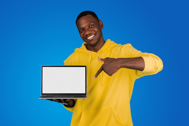 Un joven negro sonriente señala con el dedo una computadora portátil con pantalla vacía