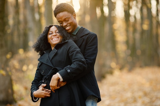 Joven negro y su novia abrazándose. Pareja romántica caminando en el parque de otoño. Hombre y mujer con abrigos negros.