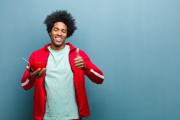 Joven negro con un tazón de desayuno contra la pared azul del grunge