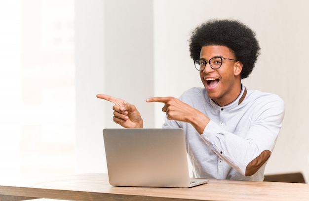 Joven negro usando su computadora portátil apuntando hacia el lado con el dedo