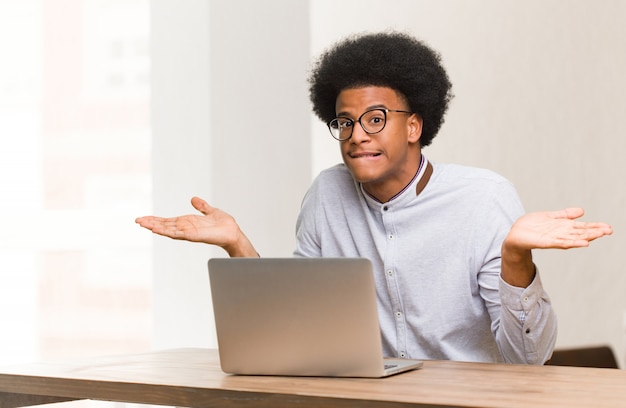 Joven negro usando su laptop confundido y dudoso