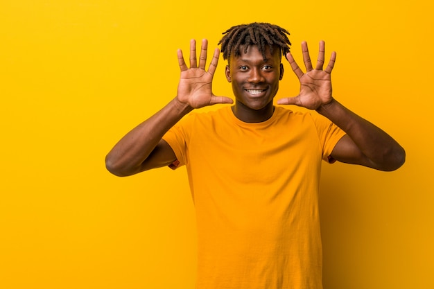 Joven negro vistiendo rastas mostrando el número diez con las manos.