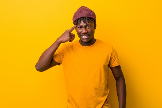 Joven negro vistiendo rastas sobre fondo amarillo mostrando un gesto de decepción con el dedo índice.