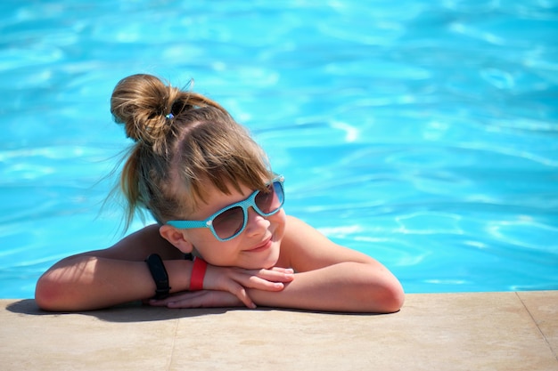 Foto joven niña alegre descansando al lado de la piscina con agua azul clara en un día soleado de verano concepto de vacaciones tropicales