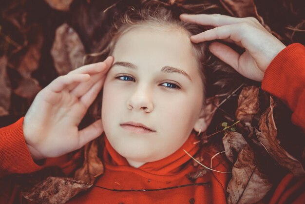 Joven niña de belleza con ojos azules tirada en la hierba cubierta de hojas