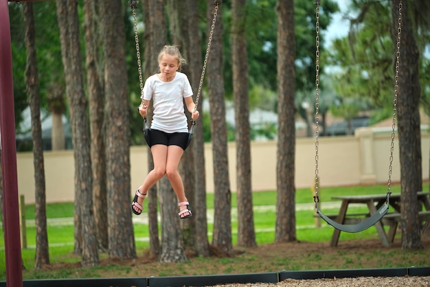 Joven niña feliz jugando sola volando alto en columpios el fin de semana de verano día soleado Seguridad y recreación en el concepto de patio de recreo