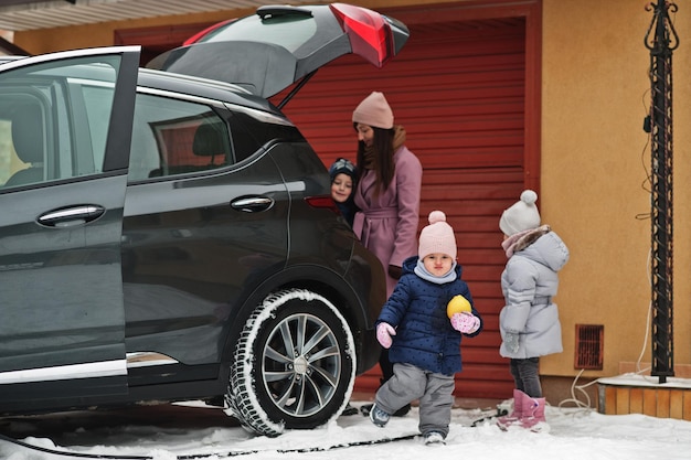 Una joven con niños sostiene bolsas ecológicas y carga un auto eléctrico con el baúl abierto en el patio de su casa