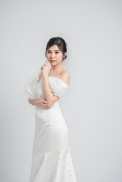 Joven novia asiática en vestido de novia sobre fondo gris