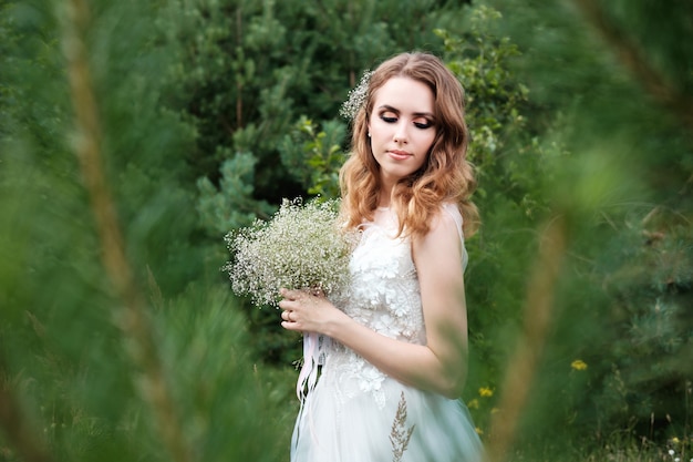 Joven novia bonita en vestido de novia blanco al aire libre, maquillaje y peinado