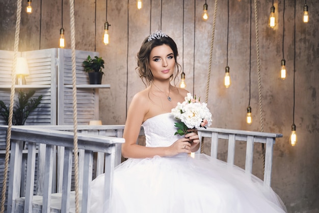 Joven novia feliz vistiendo un hermoso vestido exuberante en la habitación con muchas bombillas