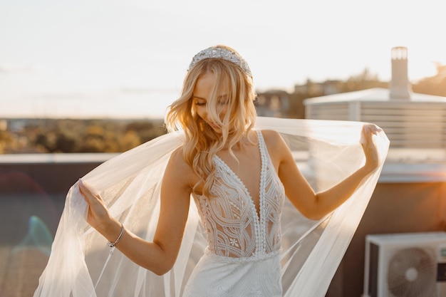 Foto joven novia rubia, maquillaje de boda, mirada feliz. hermosa mujer posando en vestido de novia blanco y velo de novia. retrato de boda. modelo de moda nupcial posando en el techo. retrato de mujer hermosa