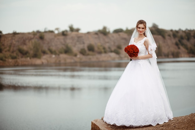 Una joven novia sonriente y hermosa con un vestido blanco está de pie