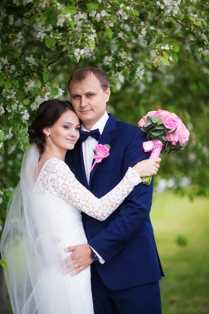 Joven novio y novia con ramo de novia en jardín floreciente