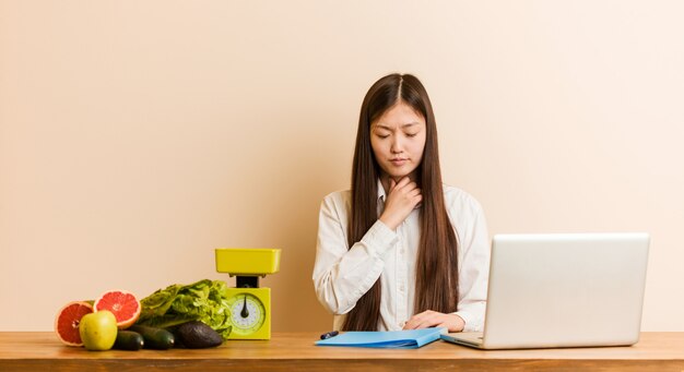 La joven nutricionista china que trabaja con su computadora portátil sufre dolor en la garganta debido a un virus o infección.