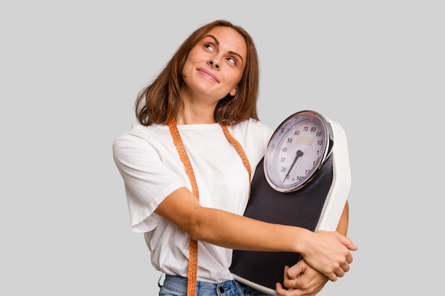 Joven nutricionista mujer caucásica sosteniendo báscula y cinta métrica aislada