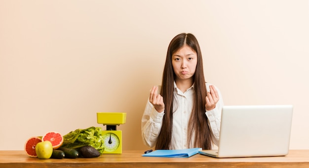 Joven nutricionista mujer china que trabaja con su computadora portátil que muestra que no tiene dinero.