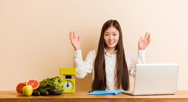 Joven nutricionista mujer china que trabaja con su computadora portátil recibiendo una agradable sorpresa