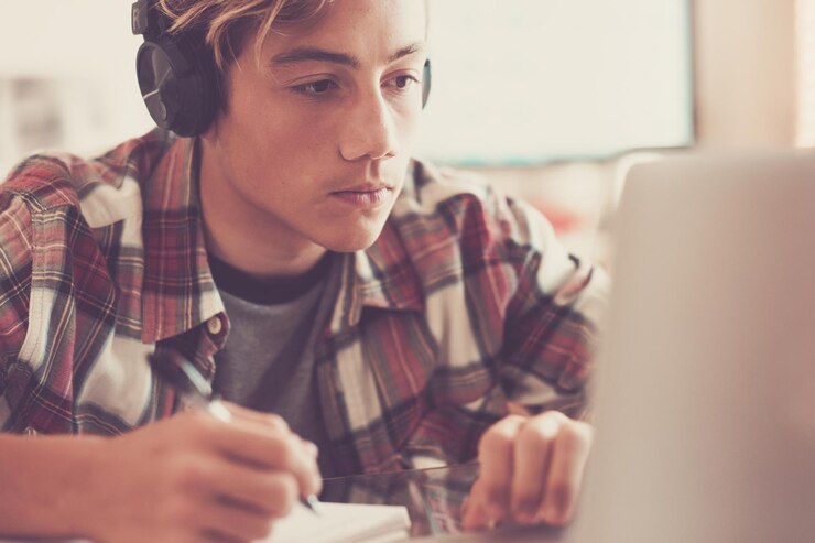 Foto un joven o adolescente que estudia y hace la tarea con una computadora portátil solo en casa milenario siguiendo clases en línea de la escuela para el encierro hermoso hombre escuchando música y relajándose