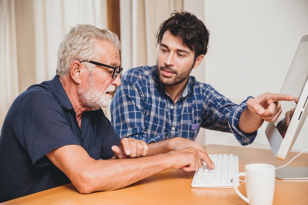 Joven o hijo enseñando a su abuelo padre anciano aprendiendo a usar la computadora en casa.