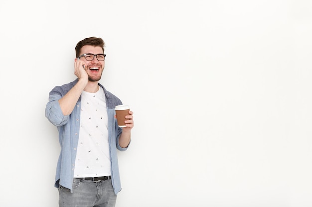 Joven ocupado hablando por teléfono con taza de café. Retrato de hombre seguro, estilo de vida moderno, concepto de comunicación