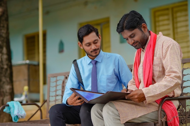 Joven oficial de banco de la India completando el papeleo con el agricultor en su casa.