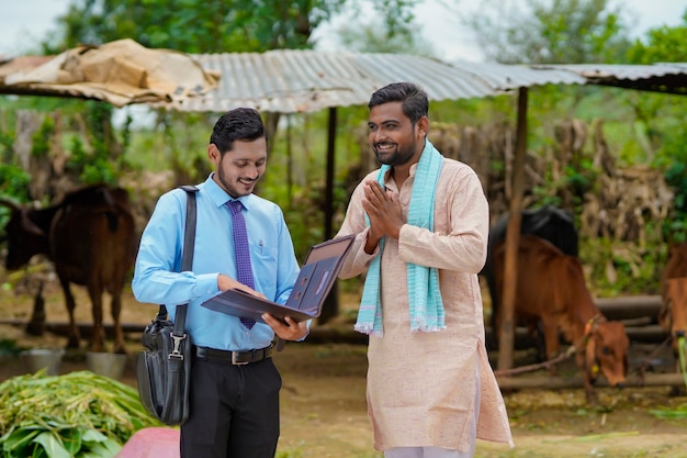 Joven oficial de banco de la India completando el papeleo con el agricultor en su granja.