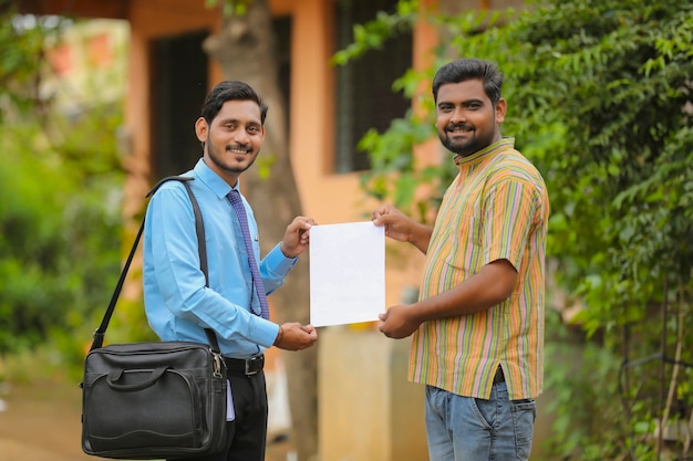 Joven oficial de banco de la india completando el papeleo y dando el certificado al agricultor.