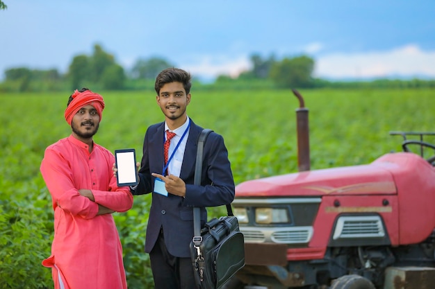 Joven oficial de banco indio y agricultor mostrando smartphone en campo agrícola