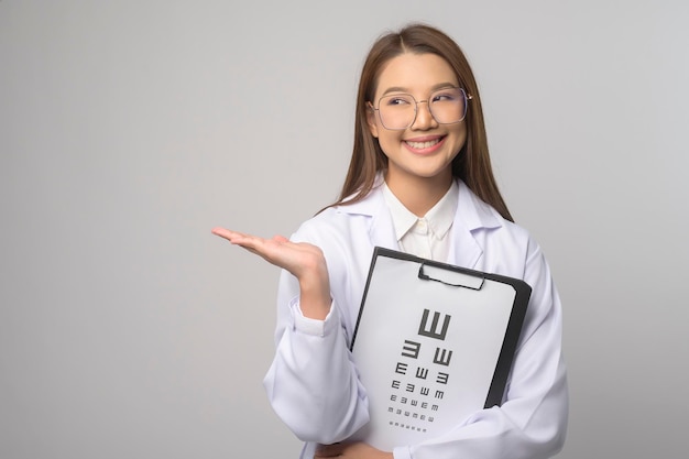 Una joven oftalmóloga con anteojos sosteniendo un gráfico optométrico sobre fondo azul.